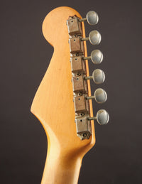 Close-up of a guitar headstock with tuning pegs on a dark background