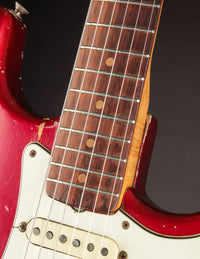 Close-up of a 1964 candy apple red Fender Stratocaster neck and fretboard against a dark background