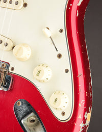 Close-up of a 1964 candy apple red Fender Stratocaster electric guitar with white pickguard and control knobs.