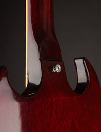 Close-up of a red electric guitar's neck with a dark background.
