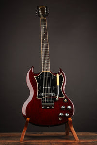 Red electric guitar on a stand against a dark background
