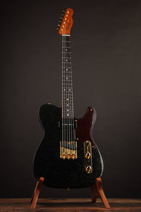 Black electric guitar on a stand against a dark background