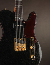 Close-up of a black electric guitar with gold hardware on a dark background