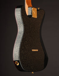 Guitar body with black glitter finish and gold hardware on a dark background