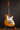 Electric guitar with a wooden body and white pickguard on a stand against a dark background