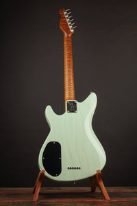 Electric guitar with a light green body and wooden neck on a stand against a dark background