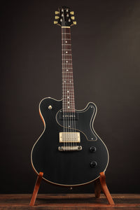 Black electric guitar on a stand against a dark background