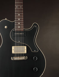 Black electric guitar with a gold pickup on a dark background