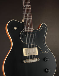 Black electric guitar with a brown pickguard on a dark background