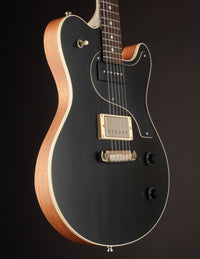 Black electric guitar with a wooden body on a dark background