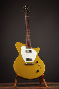 Gold electric guitar on a stand against a dark background