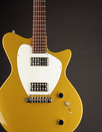 Gold electric guitar with a white pickguard on a dark background