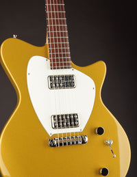 Gold electric guitar with a white pickguard on a dark background