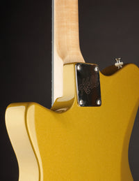 Close-up of a gold electric guitar with a visible brand logo on a dark background