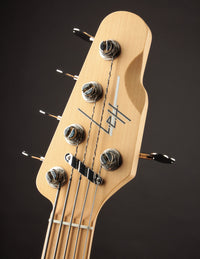 Close-up of a bass guitar headstock with tuning pegs on a dark background