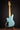 Blue electric bass guitar on a stand against a dark background, back view