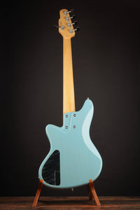 Blue electric bass guitar on a stand against a dark background, back view