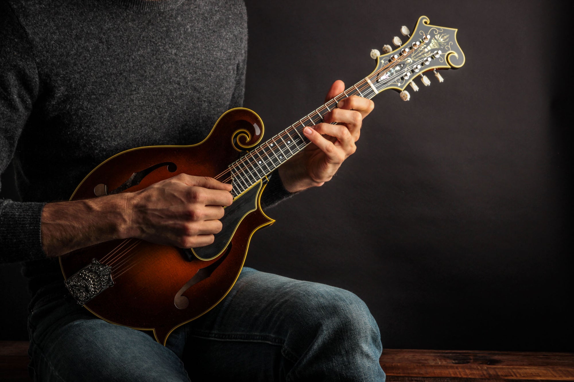 Person playing a mandolin against a dark background