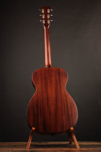 Back view of a wooden acoustic guitar on a stand against a dark background