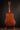 Back view of a wooden acoustic guitar on a stand against a dark background