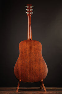 Back view of a wooden acoustic guitar on a stand against a dark background