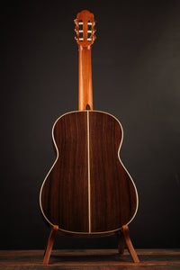 Classical acoustic guitar on a stand against a dark background, from the back