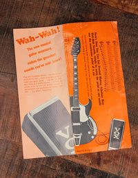 Orange advertisement for a guitar wah-wah pedal on a wooden surface