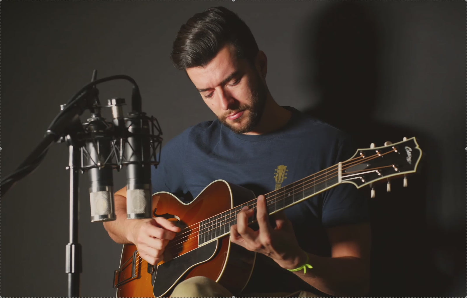 Guitarist playing a Collings AT-00 archtop against a dark background.