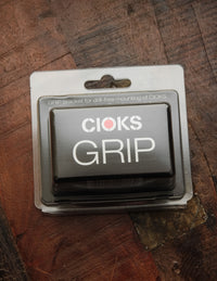 A black Cioks GRIP mounting bracket for pedalboards, packaged in a clear plastic case.