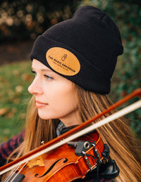 A person wearing a black TME beanie, which has a logo on the front, playing a violin.