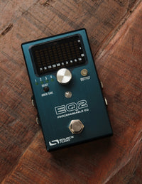 A Source Audio EQ2 Programmable EQ pedal placed on a wooden surface.